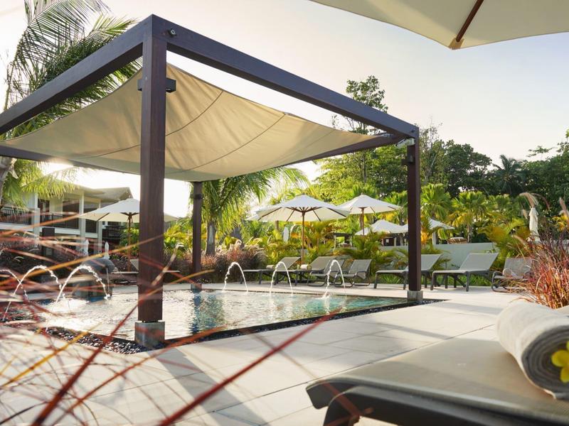 Moderner Pavillon mit Wasserbecken, Sonnenschirm und Liegestuhl in sonniger Gartenlandschaft.