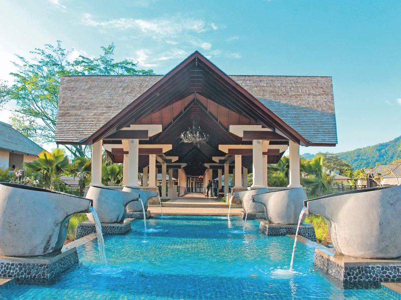 Großer offener Pavillon mit rotem Dach über blauem Pool, Wasser fließt aus Steinbrunnen.