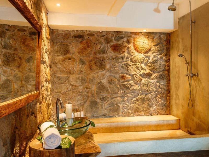 Rustikales Badezimmer mit Steinwand, großer Spiegel, Holzmöbeln und offener Dusche.