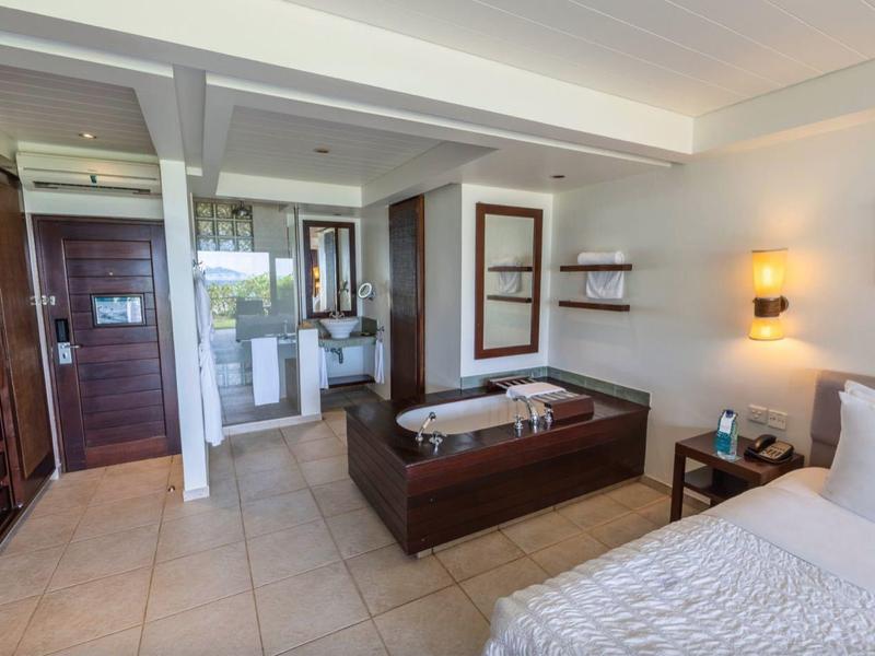 Schlafzimmer mit Fliesenboden, Doppelbett, Sofa, Kleiderschrank aus Holz und Eingangstür.