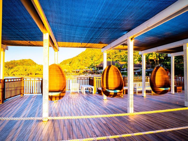 Terrasse mit hängenden Eiersesseln, weißen Säulen und Blick auf grüne Hügel im Sonnenlicht.
