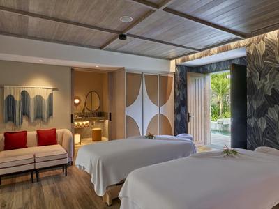 Modernes Spa-Zimmer mit zwei Massageliegen, gemütlichem Sofa, warmem Licht und natürlicher Dekoration.