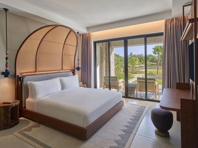 Modernes Schlafzimmer mit großem Bett, abgerundetem Kopfteil, Balkon und viel natürlichem Licht.