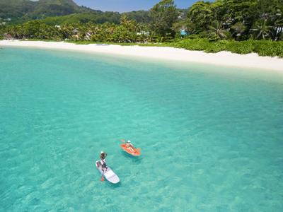 Dwie osoby pływają na deskach SUP w czystej turkusowej wodzie przy tropikalnej plaży.