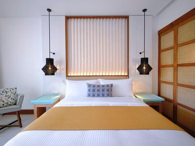 Moderní hotelový pokoj s manželskou postelí, dvěma nočními stolky a lustry inspirovanými Asií.