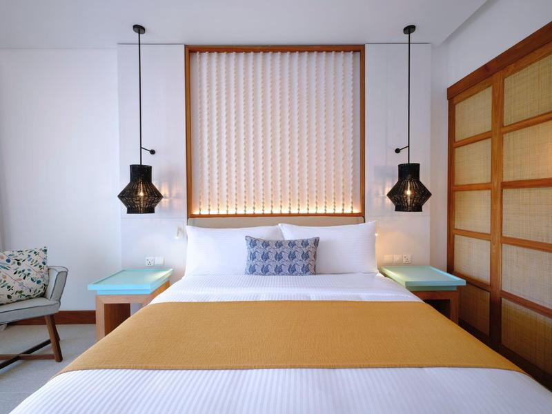 Moderní hotelový pokoj s manželskou postelí, dvěma nočními stolky a lustry inspirovanými Asií.