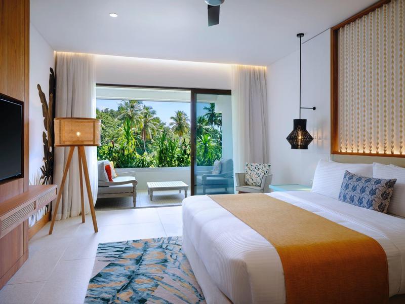 Moderní hotelový pokoj s velkou postelí, terasou a výhledem na tropickou vegetaci.