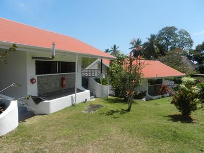 Zwei weiße Häuser mit roten Dächern stehen auf einem grünen Rasen mit einigen Bäumen und Sträuchern.