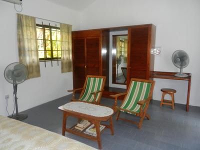 Una semplice camera d'hotel con due sedie di legno, tavolo, ventilatori e una porta dell'armadio con specchio.