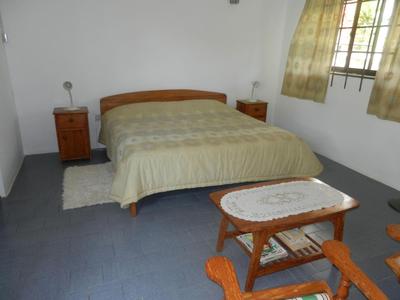 Camera semplice con letto matrimoniale, comodini e sedie in legno davanti a una finestra con tende.