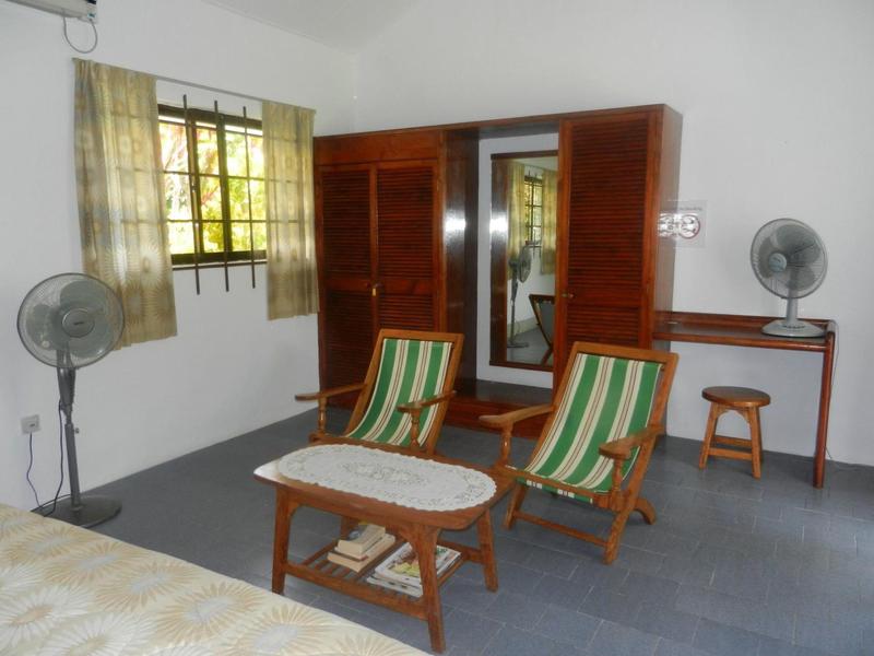 Zimmer mit zwei Sesseln, Tisch, Ventilatoren, kleinem Hocker und Schrank mit Spiegel.