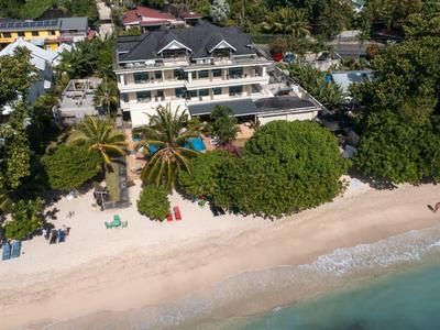 Strand mit Sand, Palmen und Liegestühlen vor einem großen, weißen Hotelgebäude mit Balkonen.