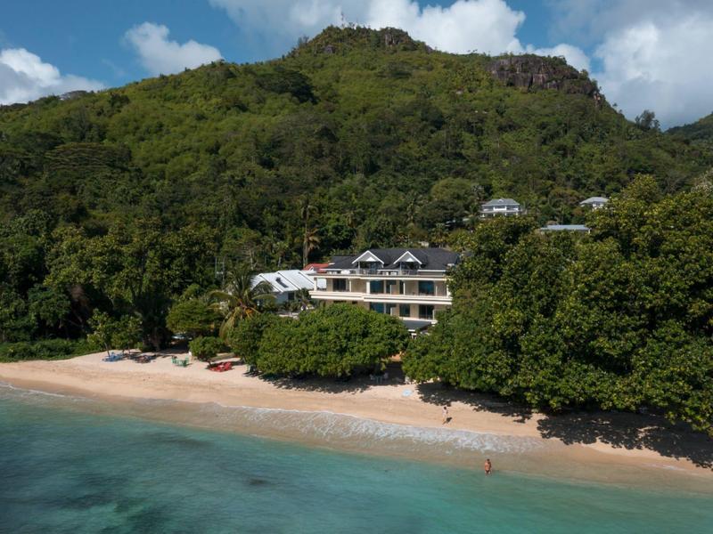 Luxury accommodation at a quiet beach with clear turquoise water in front of a forested mountain.