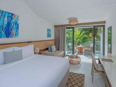 Modern hotel room with large bed, desk, balcony, and view of tropical plants.