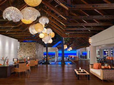 Open hotel lounge area with wooden ceiling, comfortable seating, and night sea view.