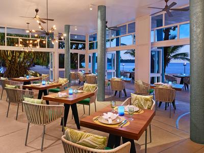 Área de restaurante moderna con mesas y sillas de madera junto a grandes ventanas con vistas al agua y botes.