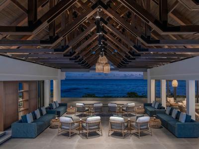 Open hotel lounge area with sea view, wooden ceiling, and modern furniture.