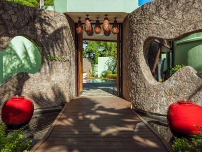 Entrance path with red cushions and round windows on a natural stone wall in a tropical hotel.