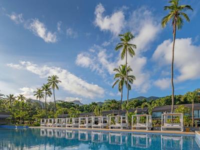 Luxuriöser Pool mit Palmen und cabana-artigen Liegeflächen unter blauem Himmel.