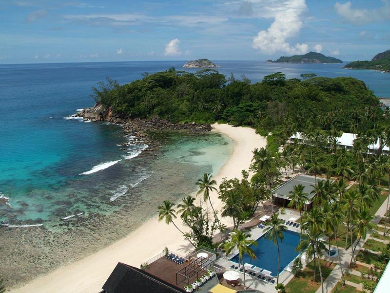 Beach with clear water, palm trees, and resort facilities on a tropical coast in sunny weather.