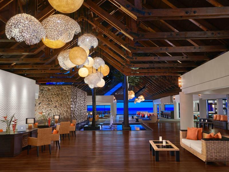 Open hotel lounge area with wooden ceiling, comfortable seating, and night sea view.