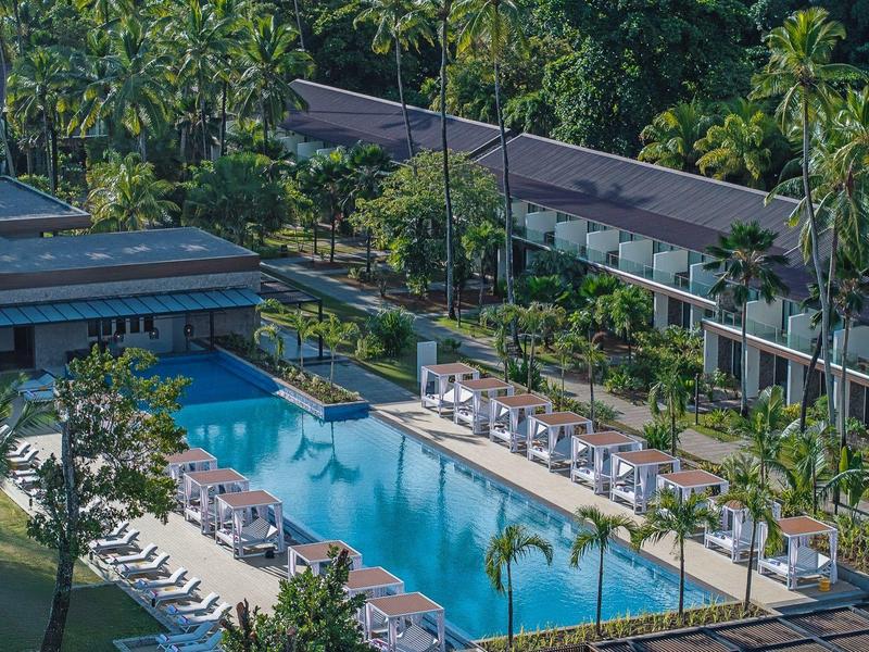 Modern outdoor pool with loungers and cabanas in tropical hotel surrounded by palm trees.
