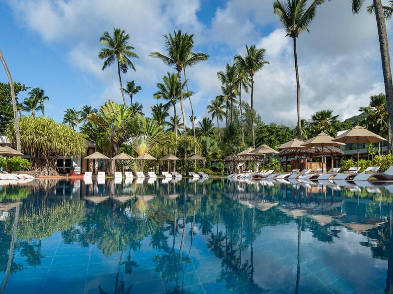 Pool area with lounge chairs and palm trees under a blue sky at a resort.