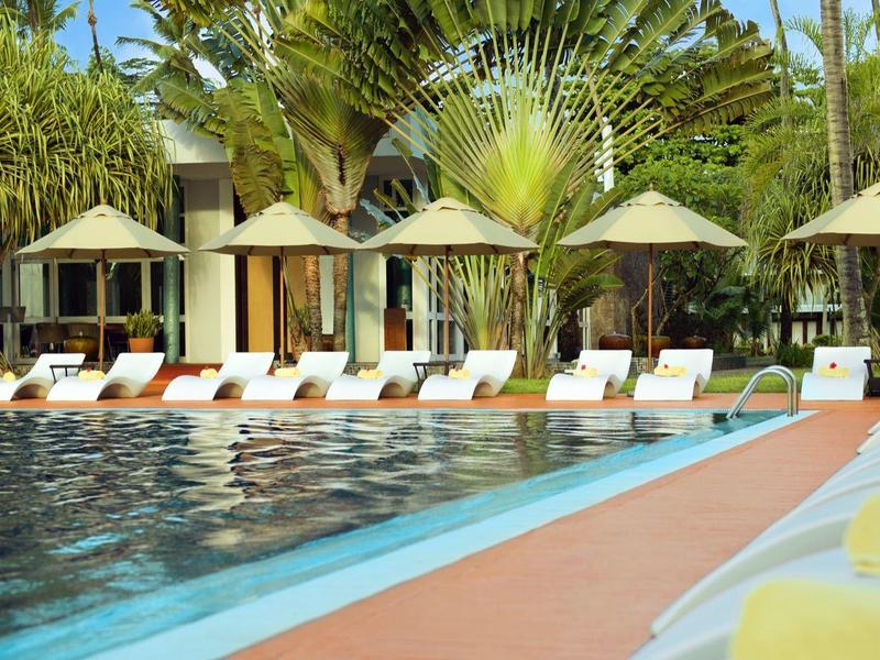 Luxury pool area with sun loungers, parasols, and tropical vegetation in the background.