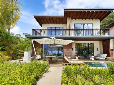 Villa de lujo con piscina, terraza y mobiliario moderno rodeada de vegetación y palmeras.