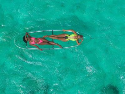 Dos personas se relajan en un kayak transparente sobre agua turquesa.