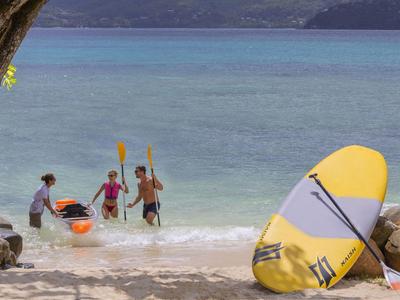 Niños en la playa preparan kayaks y juegan en aguas poco profundas junto a tablas de surf amarillas.