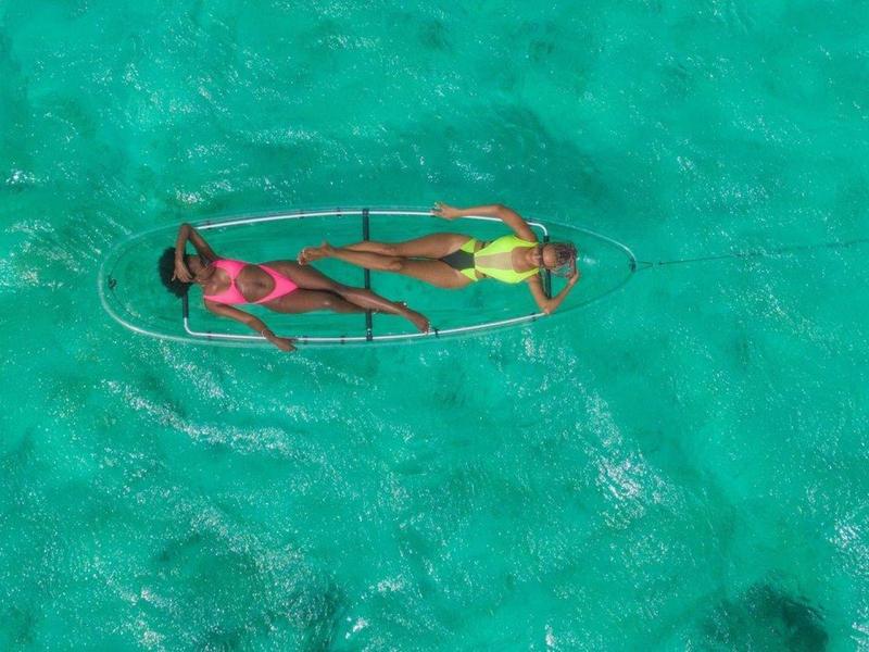 Zwei Personen liegen entspannend auf einem klaren Wasserboot im türkisfarbenen Meer.