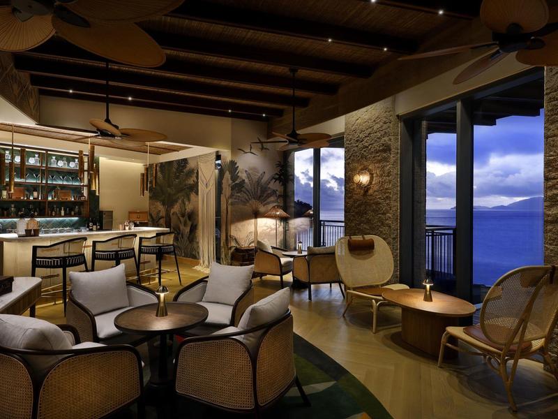 Moderner Hotel-Loungebereich mit gemütlichen Sesseln, großem Fenster mit Abendblick und Bar.