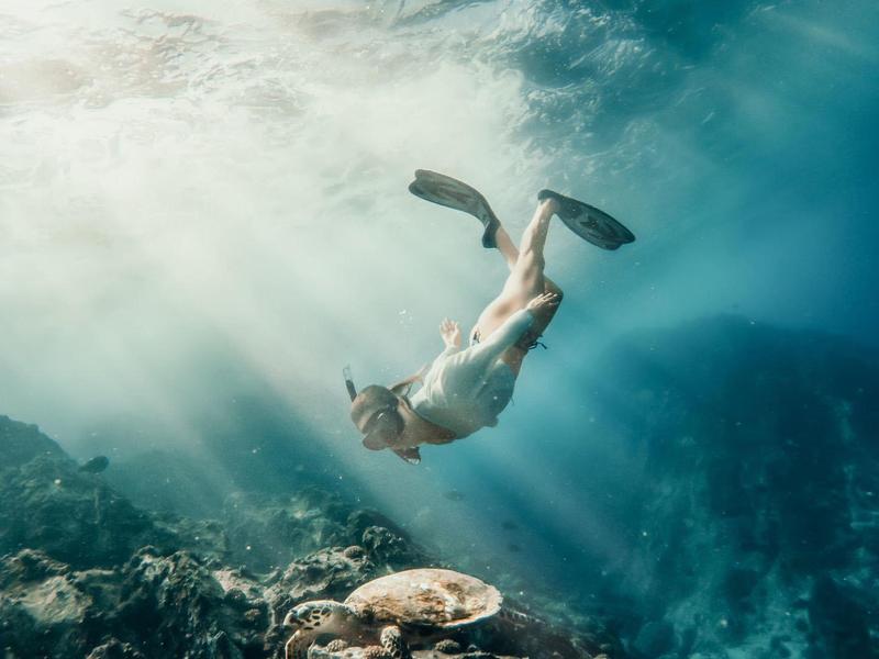 Unterwasseraufnahme eines Tauchers mit Flossen über einem Korallenriff im blauen Meer.