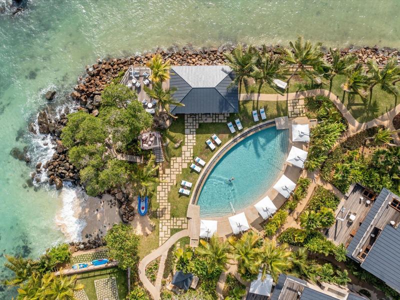 Luftaufnahme eines tropischen Resorts mit Pool, Palmen und angrenzendem Meer.