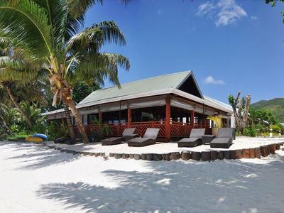 Luksusowa willa na plaży z palmami i białym piaskiem pod niebieskim niebem.