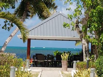 Otwarty pawilon z krzesłami nad morzem, otoczony palmami i roślinami.