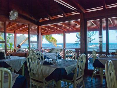 Restauracja z drewnianym dachem, białymi krzesłami i stołami z niebieskimi obrusami z widokiem na morze