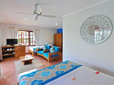 Jasny pokój hotelowy z łóżkiem, niebieskimi poduszkami na sofie i dekoracyjnym lustrem ściennym w nowoczesnym stylu.