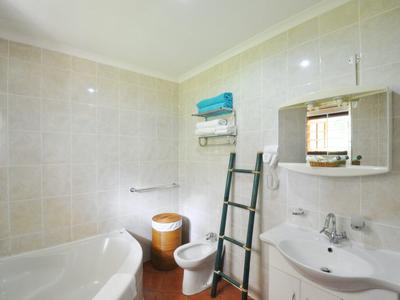 Jasna łazienka z wanną, toaletą, umywalką i lustrem z półką.