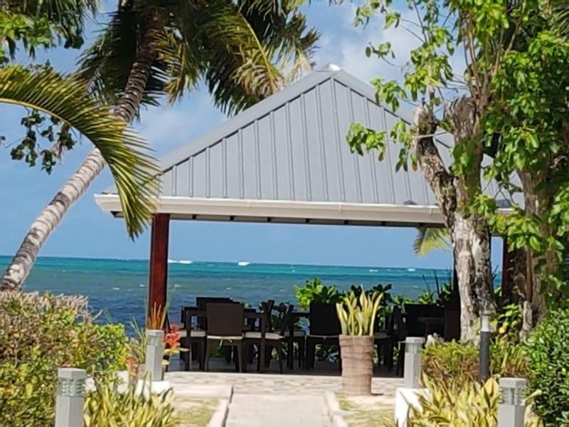 Otwarty pawilon z krzesłami nad morzem, otoczony palmami i roślinami.