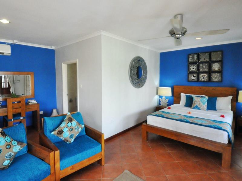 Nowoczesny pokój hotelowy z niebieskimi akcentami, podwójnym łóżkiem i wygodnymi fotelami.