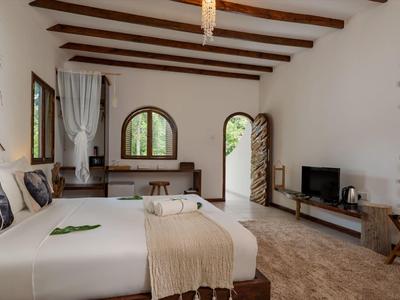 Spacious hotel room with wooden beams, two beds, TV, and nature views through windows and door.