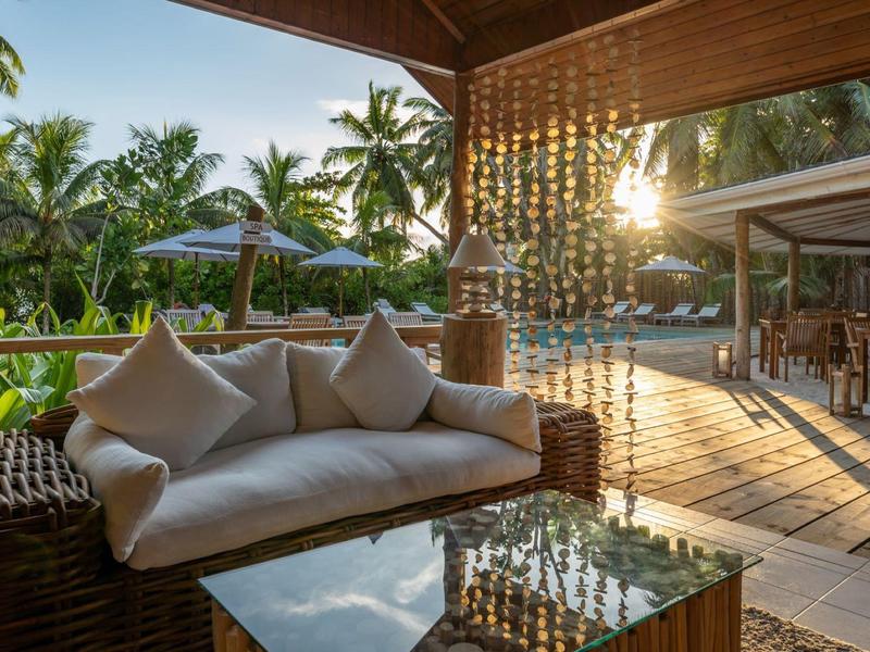 Cozy terrace with hanging sofa and view of tropical greenery at sunset.