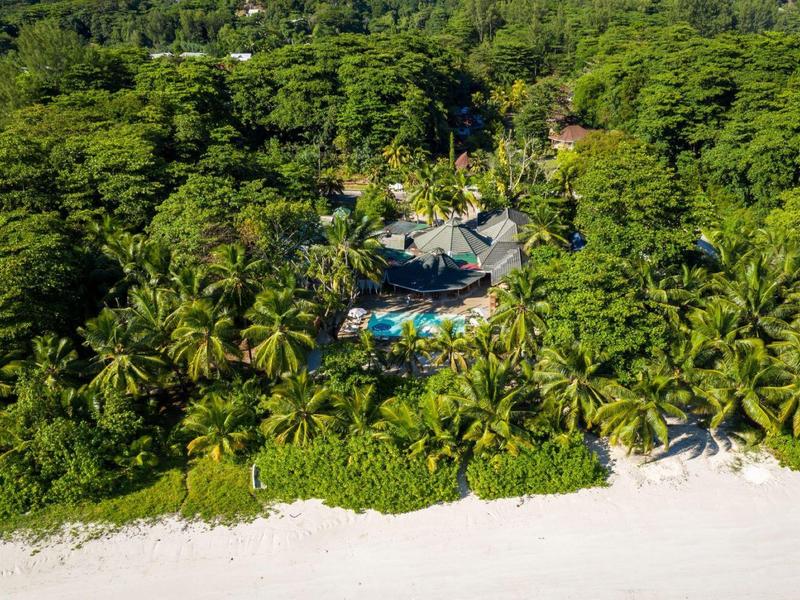 A hotel with a pool surrounded by dense, green tropical forest on a white sandy beach.