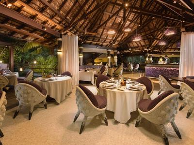 Elegantes Restaurant mit runden Tischen und bequemen Sesseln unter einem hohen Holzdach.