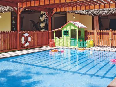 Área de juegos infantiles con piscina, casita de colores y zona soleada con sombra de vigas.