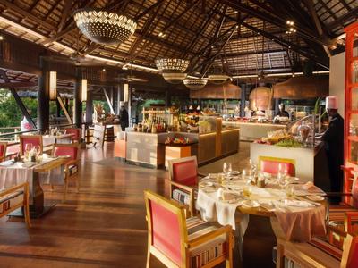 Restaurante elegante con techo de madera, araña, sillas rojas y mesas con vista al mar.