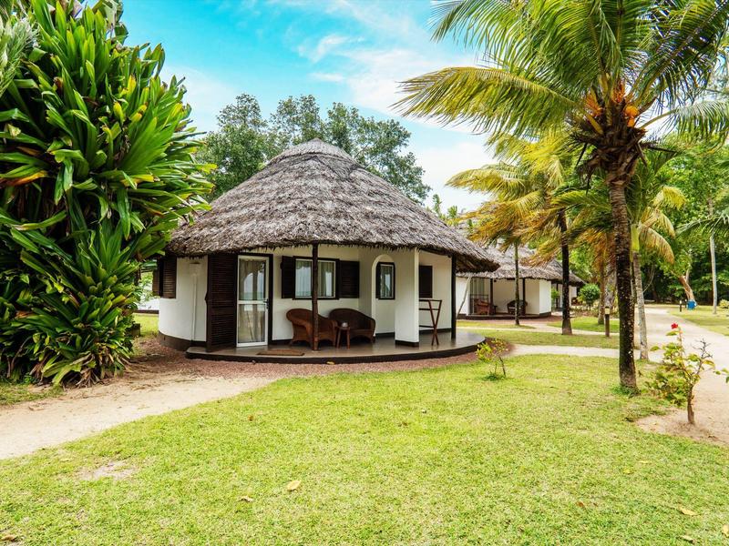 Bungalow rotondo con tetto di paglia e veranda in legno in un giardino tropicale.