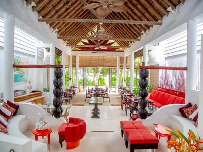 Offener Hotel-Loungebereich mit weißen Sofas, roten Akzenten und hoher Holzdecke mit Ventilatoren.